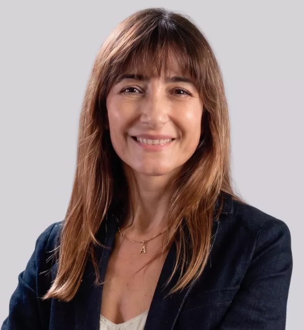 Smiling woman with shoulder-length brown hair wearing a dark blazer and a gold pendant necklace.