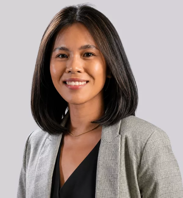 Smiling Asian woman with shoulder-length black hair wearing a gray plaid blazer over a black top, against a light gray background.