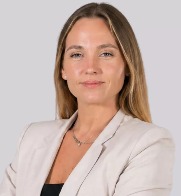Professional woman with blonde hair in a light blazer and subtle necklace, facing the camera with a slight smile in a neutral studio backdrop.