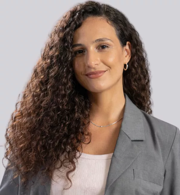 Professional portrait of a woman with long, voluminous curly brown hair, wearing a gray blazer and light top, smiling at the camera.